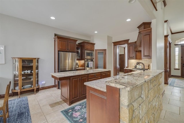 kitchen featuring light stone countertops, a peninsula, stainless steel appliances, tasteful backsplash, and a center island