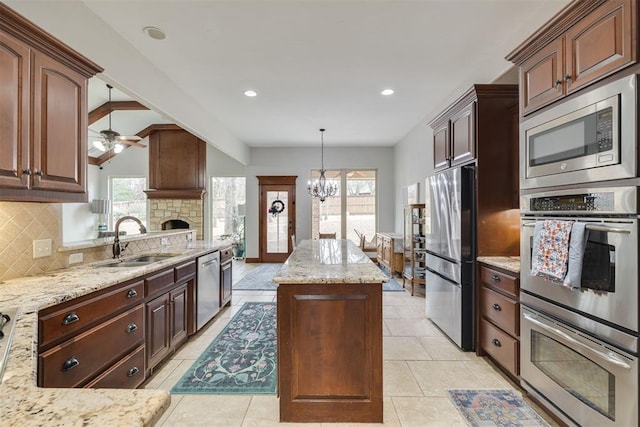 kitchen featuring light stone countertops, a sink, appliances with stainless steel finishes, backsplash, and a center island