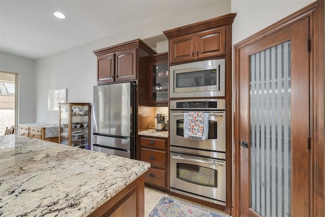 kitchen with light tile patterned floors, appliances with stainless steel finishes, glass insert cabinets, and light stone countertops