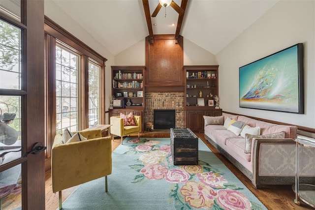 living area featuring wood finished floors, vaulted ceiling with beams, a fireplace, and ceiling fan