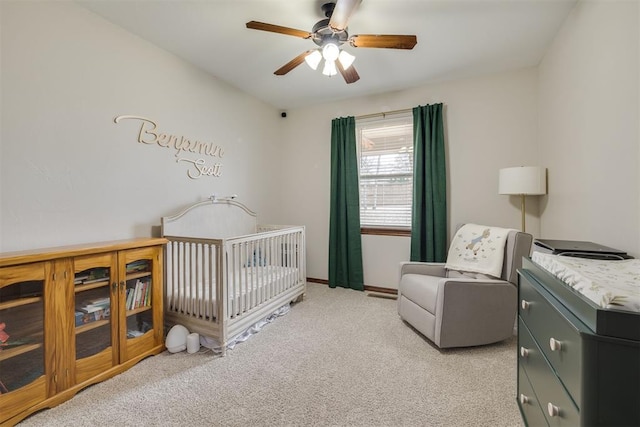 bedroom with baseboards, light carpet, a nursery area, and a ceiling fan