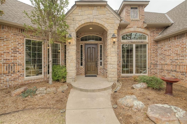 doorway to property featuring brick siding and roof with shingles