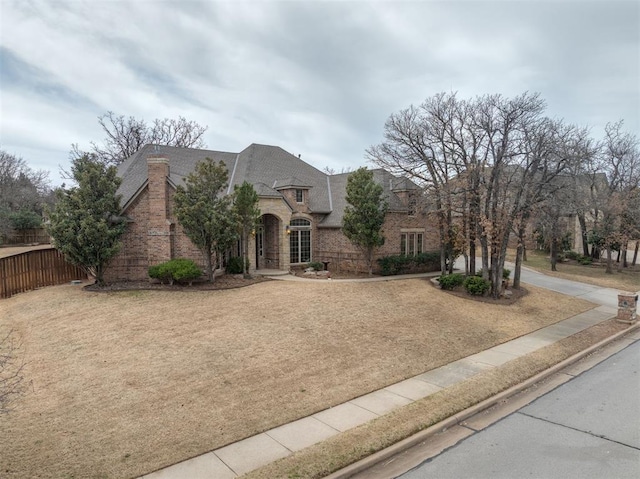 view of front facade with brick siding, stone siding, a front yard, and fence