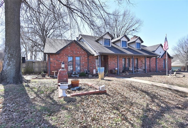 cape cod home with brick siding, a shingled roof, and fence