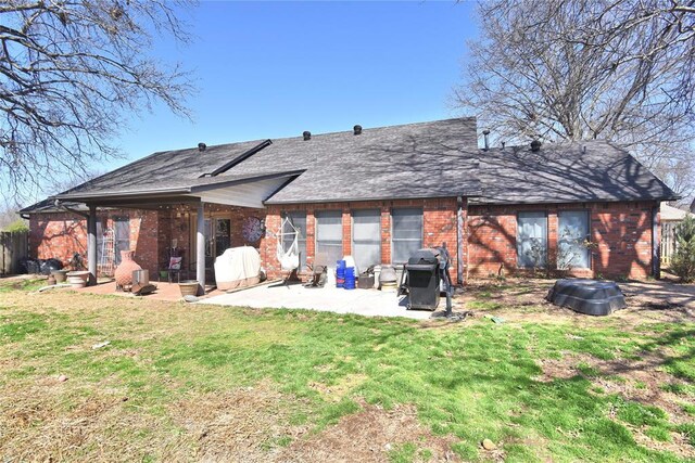 rear view of property featuring a patio, a lawn, roof with shingles, and brick siding