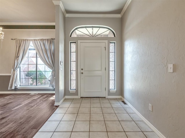 foyer entrance featuring crown molding, a textured wall, baseboards, and light wood finished floors