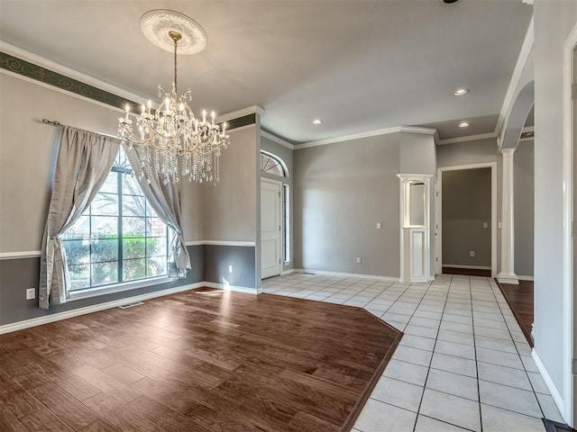 unfurnished dining area featuring visible vents, crown molding, baseboards, a chandelier, and arched walkways