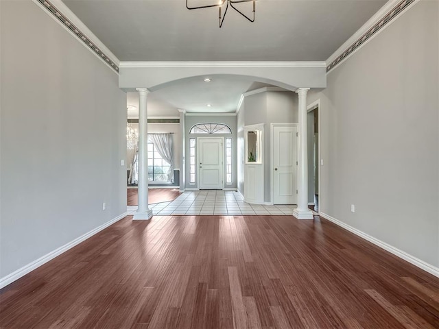 foyer featuring crown molding, decorative columns, wood finished floors, and baseboards