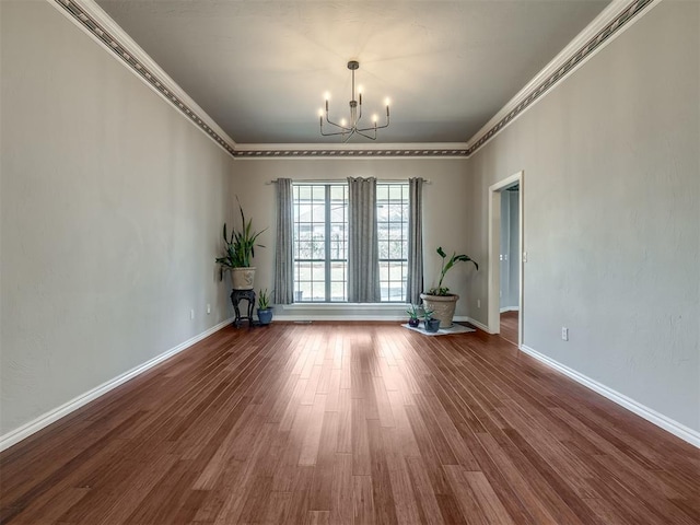 unfurnished room with baseboards, a notable chandelier, wood finished floors, and crown molding