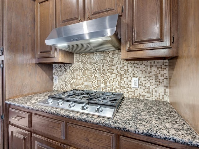 kitchen featuring under cabinet range hood, dark stone counters, backsplash, and stainless steel gas stovetop