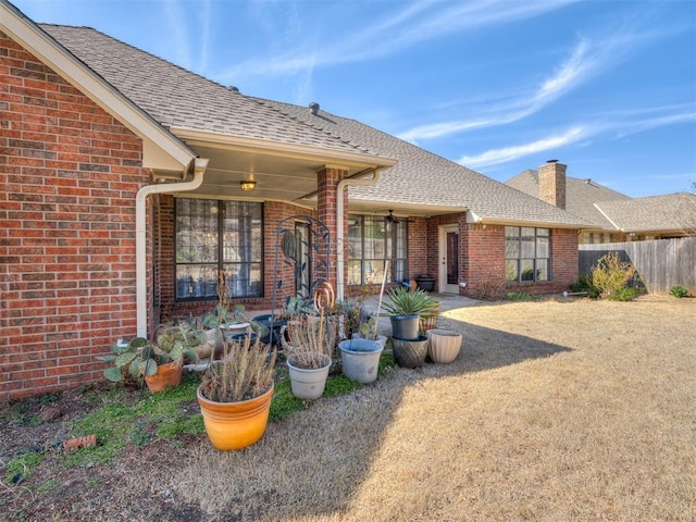 rear view of house featuring brick siding, a chimney, and fence