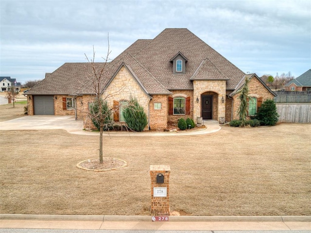 french country inspired facade with a shingled roof, fence, concrete driveway, a garage, and stone siding