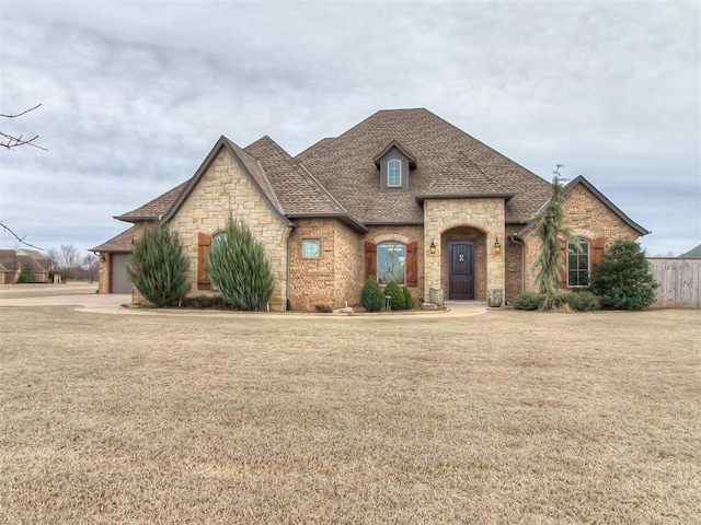 french country inspired facade with stone siding, a shingled roof, and a front lawn