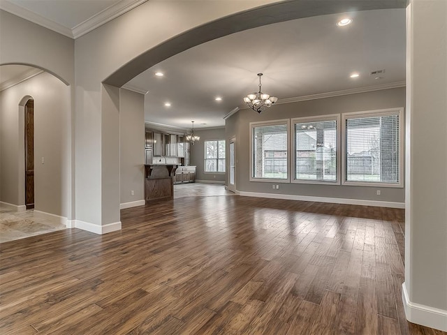 unfurnished living room featuring ornamental molding, arched walkways, an inviting chandelier, baseboards, and dark wood-style flooring