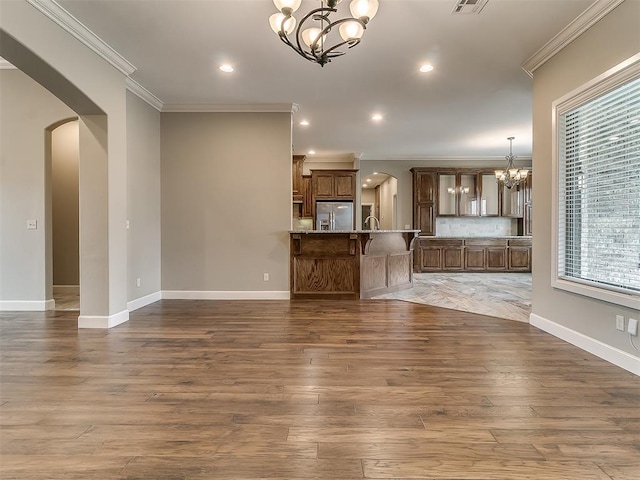 unfurnished living room with baseboards, ornamental molding, wood finished floors, arched walkways, and a notable chandelier