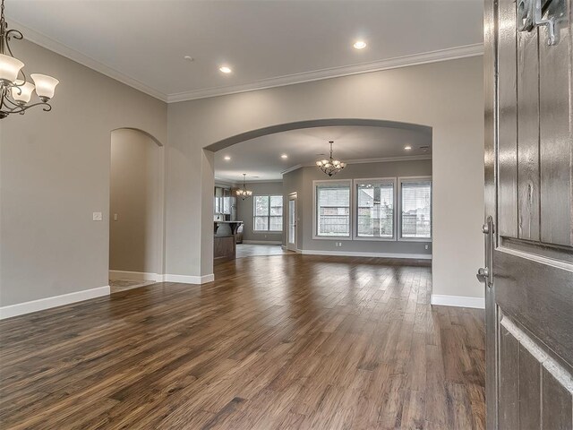 unfurnished living room with baseboards, arched walkways, an inviting chandelier, and dark wood-style floors