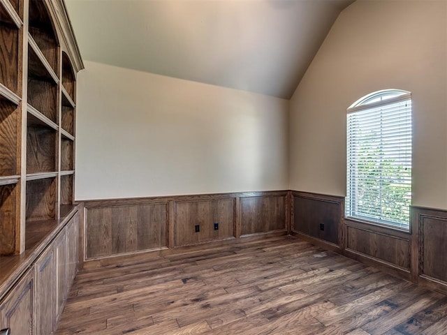 unfurnished room featuring lofted ceiling, wood finished floors, and wainscoting