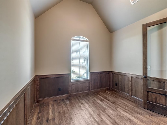 spare room featuring lofted ceiling, wood finished floors, and wainscoting