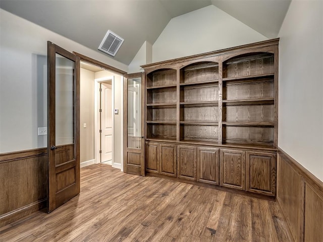 spare room featuring visible vents, a wainscoted wall, dark wood finished floors, and vaulted ceiling