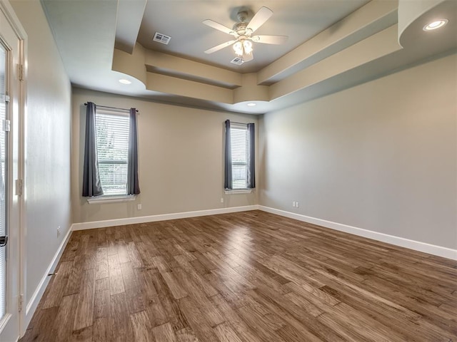 empty room featuring a ceiling fan, wood finished floors, visible vents, a tray ceiling, and plenty of natural light