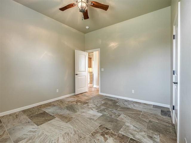 spare room featuring baseboards, ceiling fan, and stone finish floor