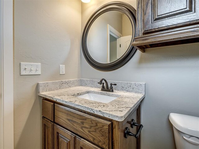 bathroom with vanity, toilet, and a textured wall