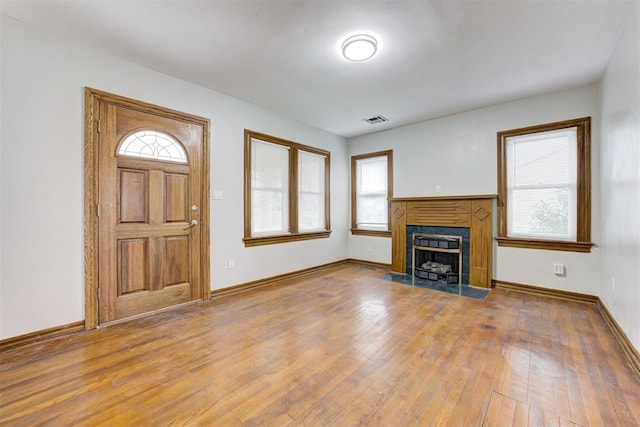 unfurnished living room featuring visible vents, a fireplace with flush hearth, baseboards, and hardwood / wood-style flooring