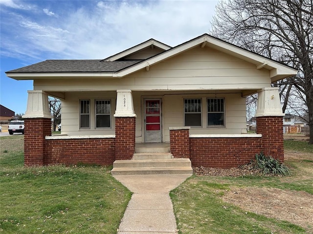 bungalow-style house featuring brick siding, covered porch, a shingled roof, and a front lawn