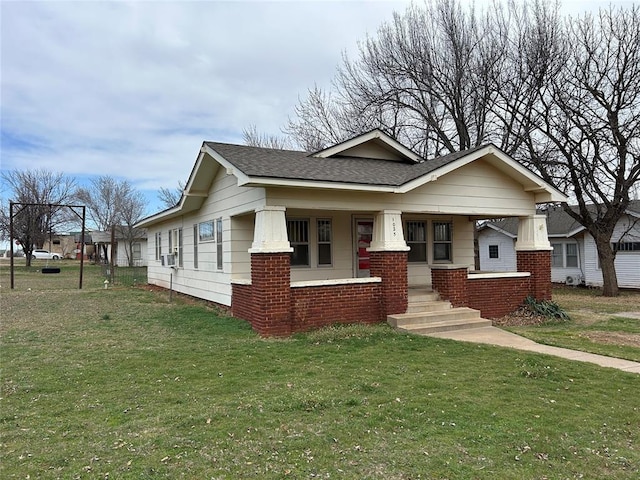 view of front facade featuring brick siding, a porch, a front yard, and roof with shingles