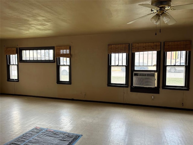 empty room with cooling unit, baseboards, light floors, and a ceiling fan