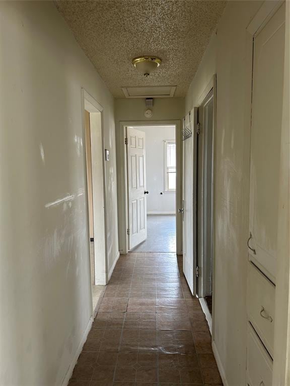 hall featuring baseboards, a textured ceiling, and attic access