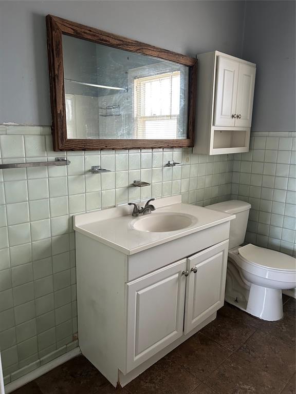 bathroom featuring toilet, vanity, and tile walls