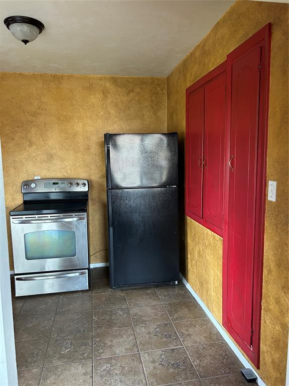 kitchen featuring stainless steel electric range, freestanding refrigerator, baseboards, and reddish brown cabinets