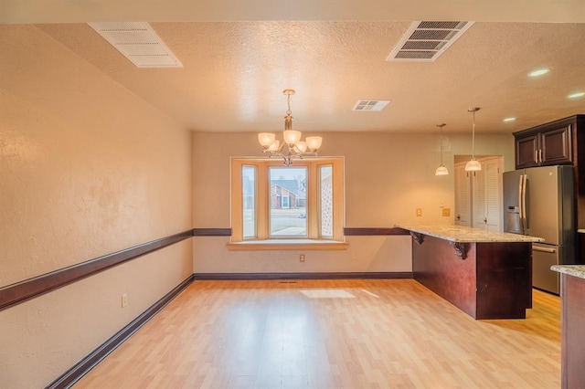 kitchen with a kitchen bar, visible vents, stainless steel refrigerator with ice dispenser, light wood-style floors, and a chandelier