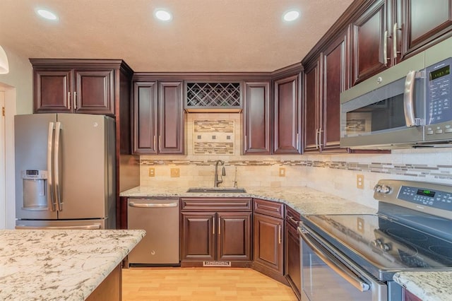 kitchen featuring a sink, stainless steel appliances, light stone countertops, and light wood-style flooring