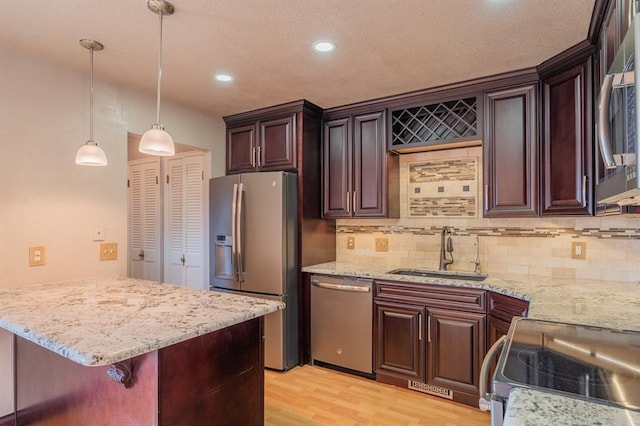 kitchen featuring light stone countertops, light wood-style floors, hanging light fixtures, stainless steel appliances, and a sink