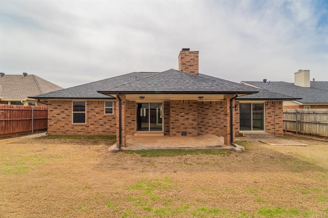 rear view of property featuring brick siding, roof with shingles, a fenced backyard, and a patio area