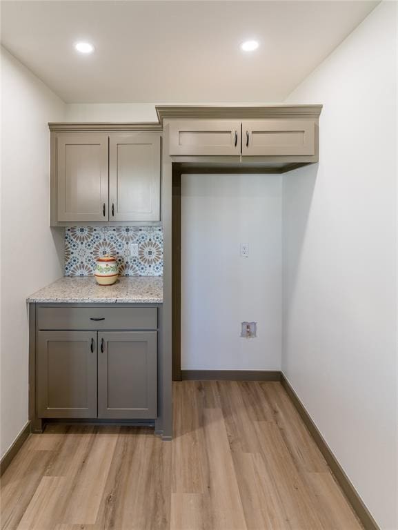 kitchen featuring light stone countertops, baseboards, gray cabinets, light wood-type flooring, and backsplash