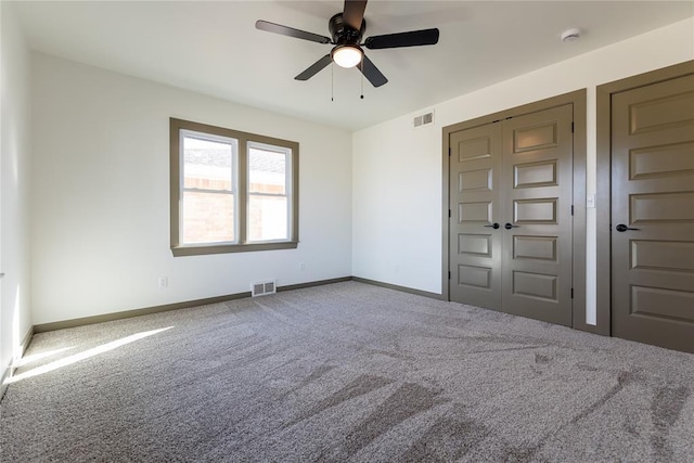 carpeted spare room with visible vents, baseboards, and ceiling fan