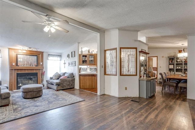 living area featuring visible vents, vaulted ceiling with beams, dark wood-style flooring, a textured ceiling, and a glass covered fireplace