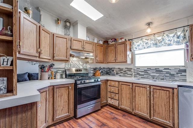 kitchen with under cabinet range hood, light countertops, lofted ceiling, appliances with stainless steel finishes, and a sink