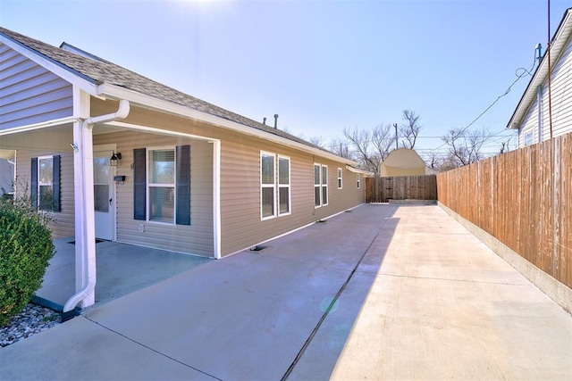 view of home's exterior featuring roof with shingles, a patio, and fence