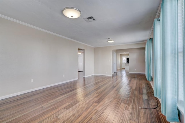 empty room with crown molding, wood finished floors, visible vents, and baseboards