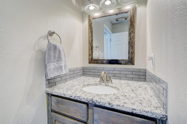 bathroom with vanity, tasteful backsplash, a textured wall, and visible vents