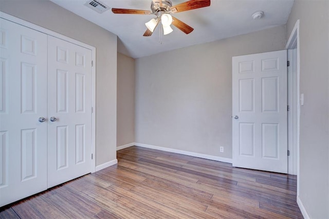 unfurnished bedroom with wood finished floors, visible vents, a closet, and baseboards