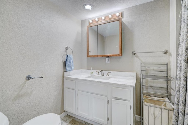 bathroom featuring a textured ceiling, toilet, vanity, and a textured wall