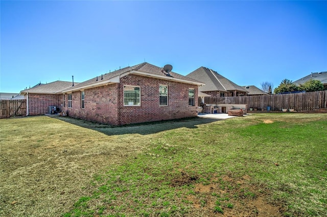 rear view of house featuring a patio area, a yard, a fenced backyard, and brick siding