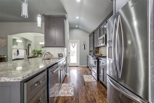 kitchen with light stone counters, arched walkways, gray cabinetry, a sink, and appliances with stainless steel finishes