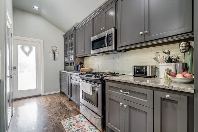 kitchen with dark wood-style flooring, gray cabinets, vaulted ceiling, appliances with stainless steel finishes, and tasteful backsplash