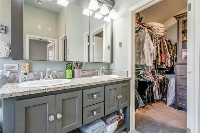 full bathroom with a walk in closet, double vanity, visible vents, and a sink